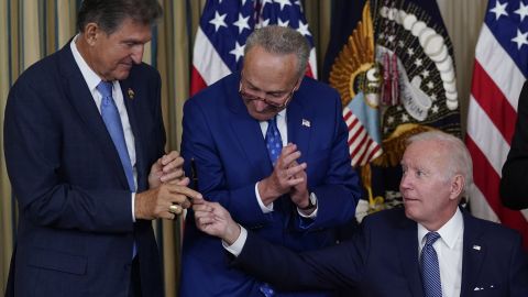 President Joe Biden hands the pen he used to sign the Democrats' landmark climate change and health care bill to Manchin as Schumer looks on.