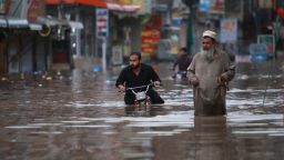 TOPSHOT - A man wades next to another pushing a motorbike along a waterlogged street after the monsoon rainfall in Rawalpindi on July 13, 2022. (Photo by Raja Imran / AFP) (Photo by RAJA IMRAN/AFP via Getty Images)