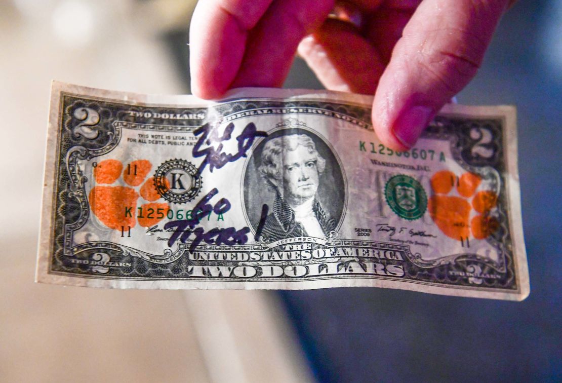 Clemson fans mark their "Tiger Two's" with orange paws from a stamp pad and spend them to give businesses on the road the idea of their economic impact.