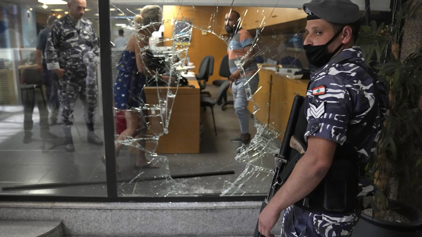 A Lebanese policeman stands guard next to a bank window that was broken by depositors who attacked it trying to get blocked money in Beirut on Wednesday, September 14, 2022. 