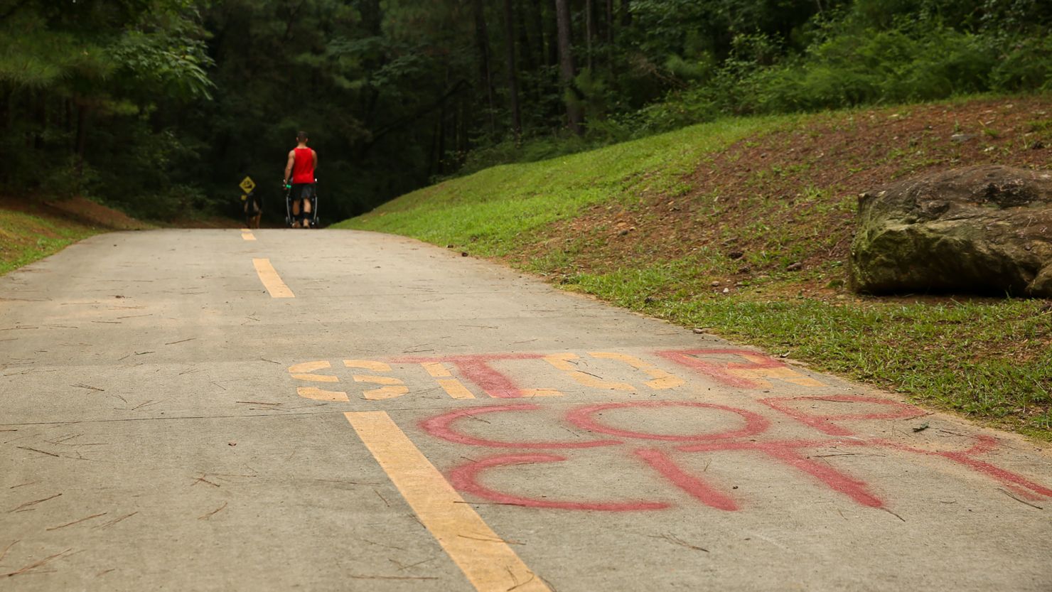 A man walks his dog along the South River Trail, which leads into Intrenchment Creek Park, in Atlanta on August 15, 2022. On the road, the words 'Stop Cop City' reflect the sentiment of advocates and residents who don't want to see a new police and fire training facility built in the area.