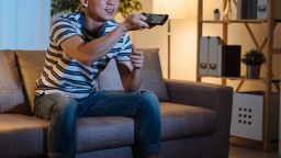 cheerful young asian chinese man watching movies on tv at home late in evening.