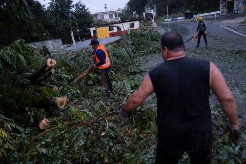 People clear a road from a fallen tree in Yauco, Puerto Rico, on Sunday.