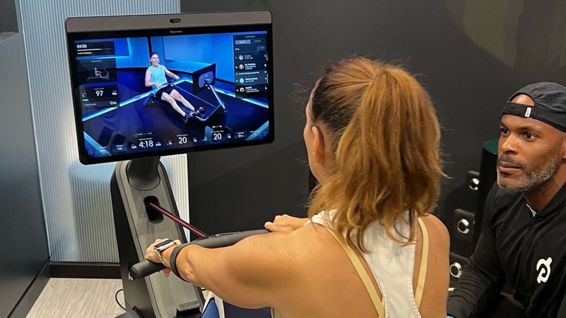 An instructor watches as a women exercises on a rowing machine.