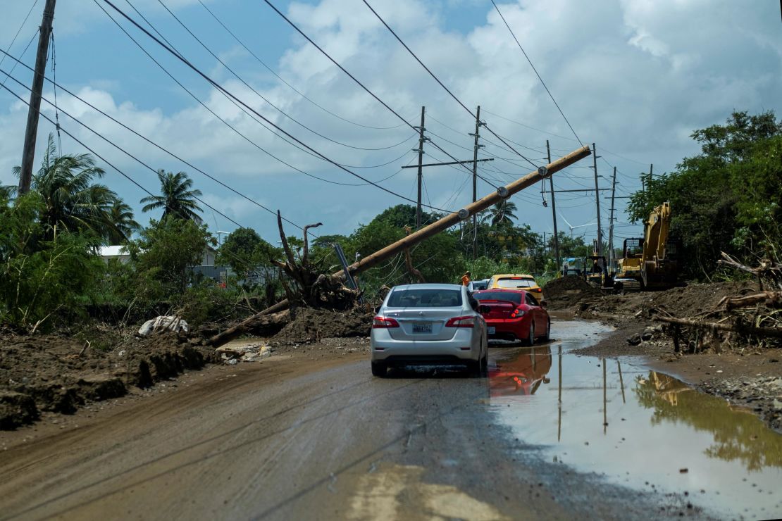 Cars drive Wednesday under a downed power pole in Santa Isabel, Puerto Rico.