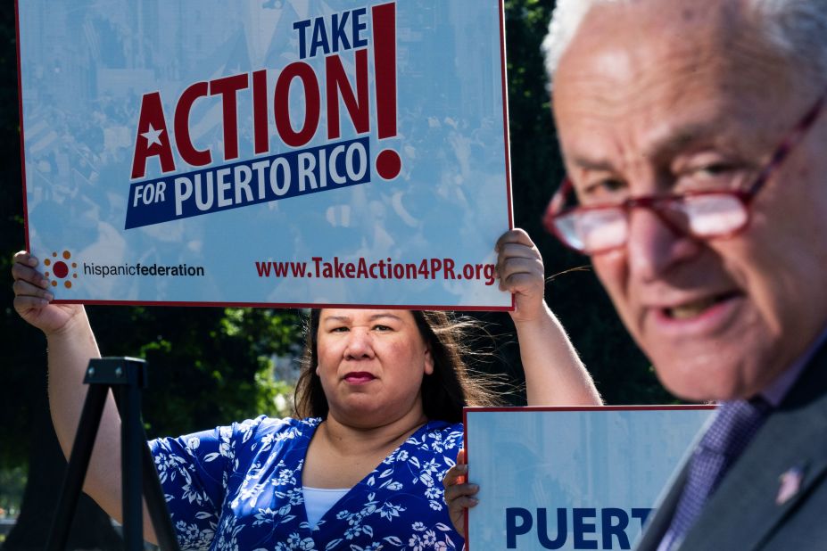 Mónica Ramírez, founder and president of the group Justice for Migrant Women, holds up a sign that reads "Take action for Puerto Rico!" as Senate Majority Leader Chuck Schumer speaks during a news conference outside the US Capitol on Tuesday, September 20. Schumer was calling for federal assistance for Puerto Rico in the wake of Hurricane Fiona.