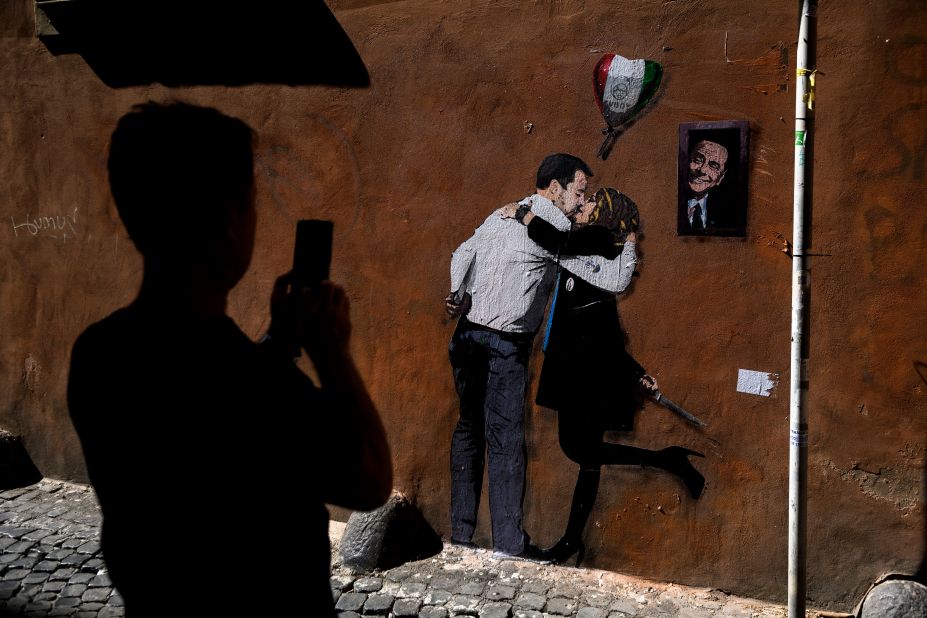 A man in Rome takes pictures of a mural, painted by the street artist Tvboy, that depicts Giorgia Meloni and Matteo Salvini, leaders of two different political parties, kissing while holding knives in their hands on Tuesday, September 20.