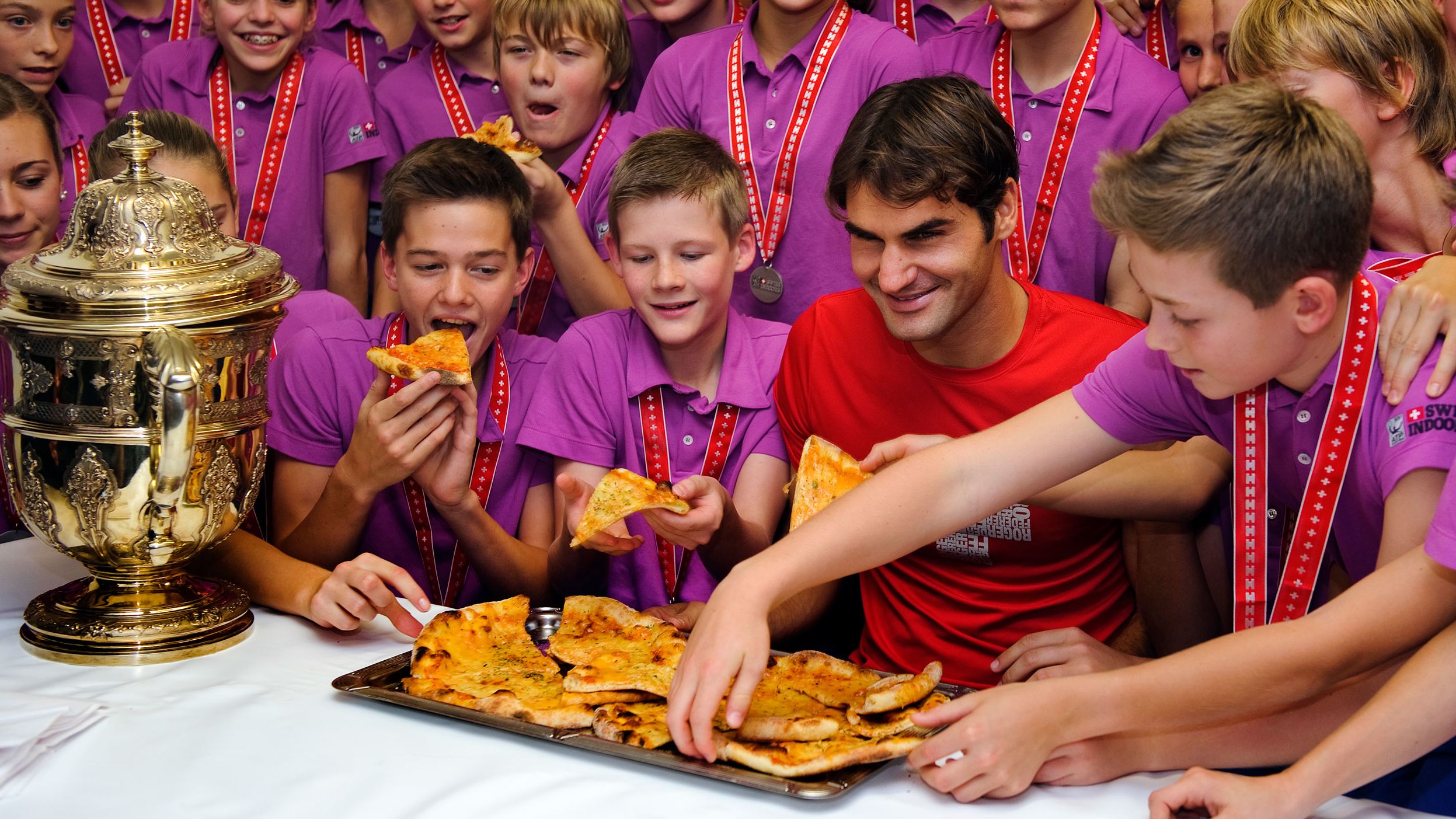 After winning a tournament in Switzerland, Federer poses with ball boys and girls as they pick up slices of pizza in 2011. Federer, who once worked as a ball boy in Basel, hosted the pizza party.