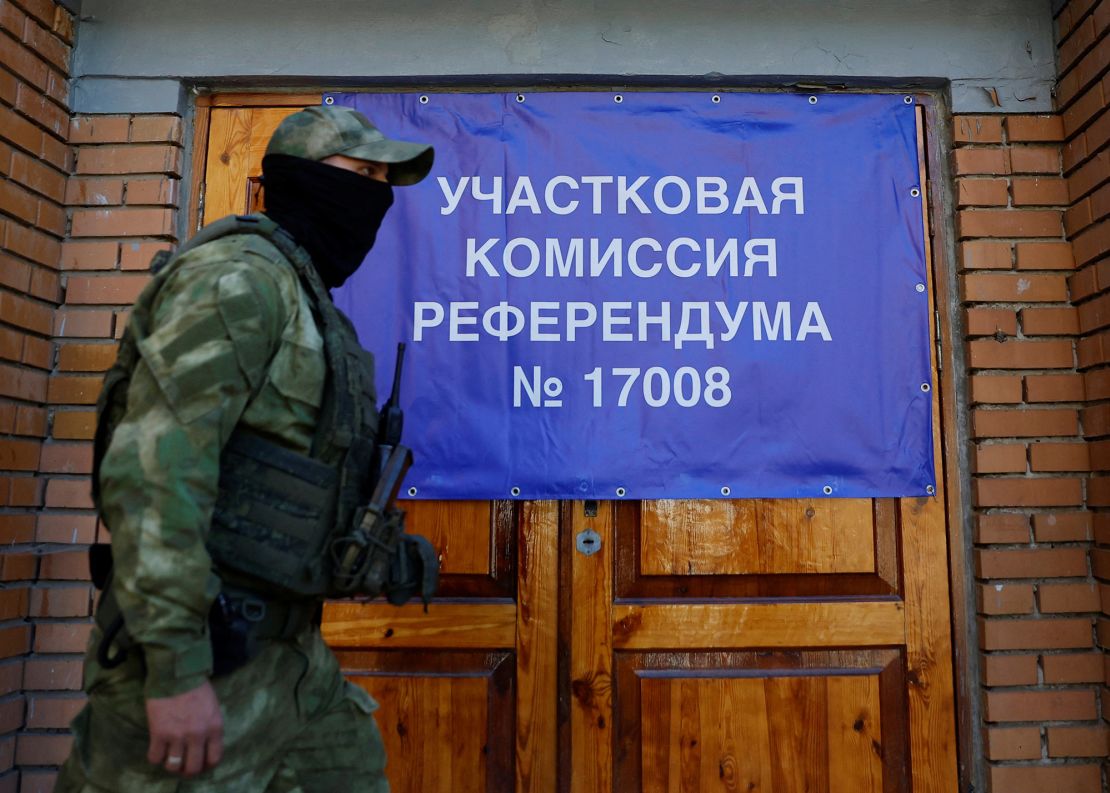 A service member of the self-proclaimed Donetsk People's Republic walks past a banner on the doors of a polling station.