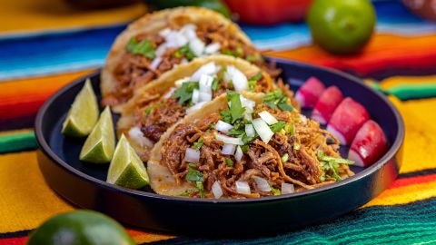 Carnitas tacos served with diced red onions, cilantro, a radish garnish and lime.