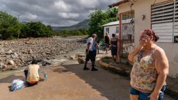 Carmen Baez becomes emotional while standing in front of where her home used to be as a boy uses her washing machine valves to collect fresh water in Guayama.