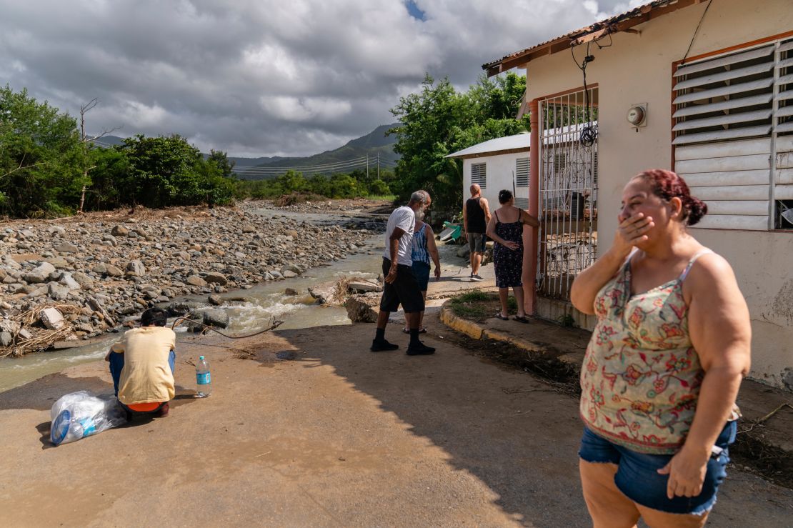 Carmen Baez becomes emotional while standing in front of where her home used to be. The boy to her right uses her washing machine valves to collect fresh water in Guayama.