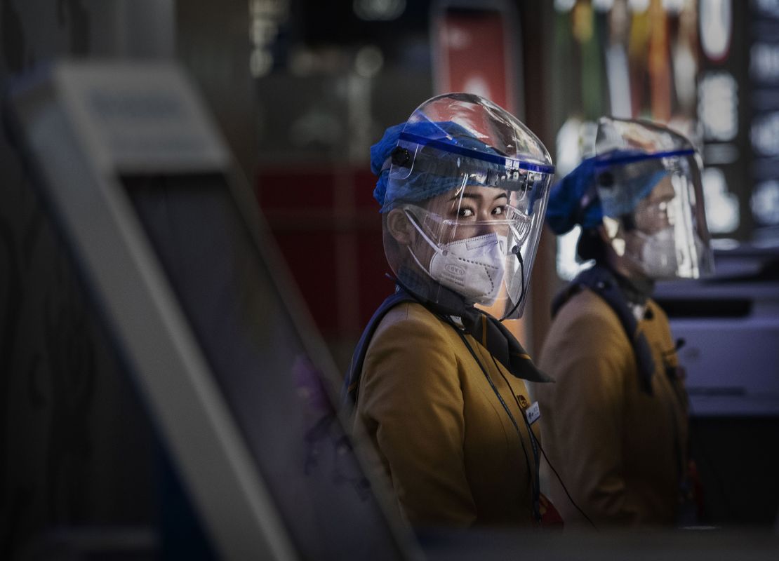 Chinese tourist information clerks wear protective masks and visors at their desk in the departures area of Beijing International Airport, March 2020. 