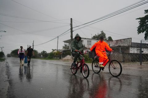 People walk and cycle through the rain ahead of Ian's arrival in Coloma, Cuba, on Monday.