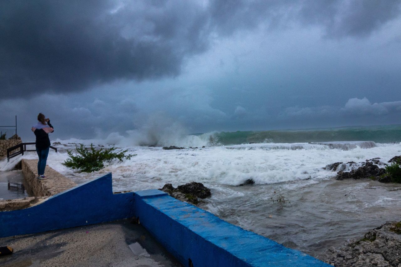 A woman takes photos while waves crash against a seawall in George Town, Grand Cayman, on Monday.