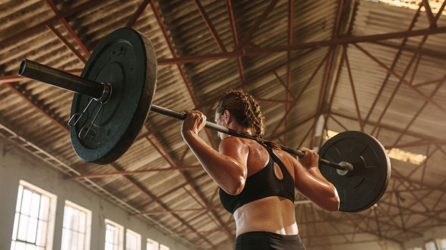 Strong woman exercising with barbell. Fit woman working out with heavy weights at cross training gym in factory shade.