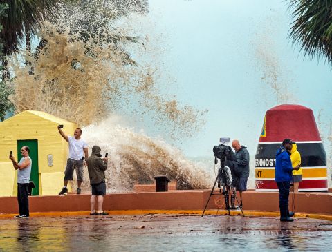 News crews, tourists and local residents take images Tuesday as high waves crash into a seawall in Key West, Florida.