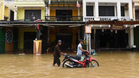 People push a motorcycle through a flooded street in Hoi An city, Quang Nam province, on September 28, 2022.