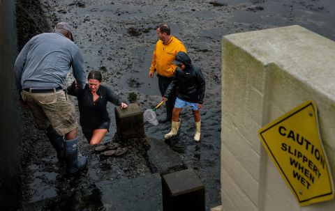 A woman is helped out of a muddy area on Wednesday in Tampa, Florida, where water was receding due to a negative storm surge.