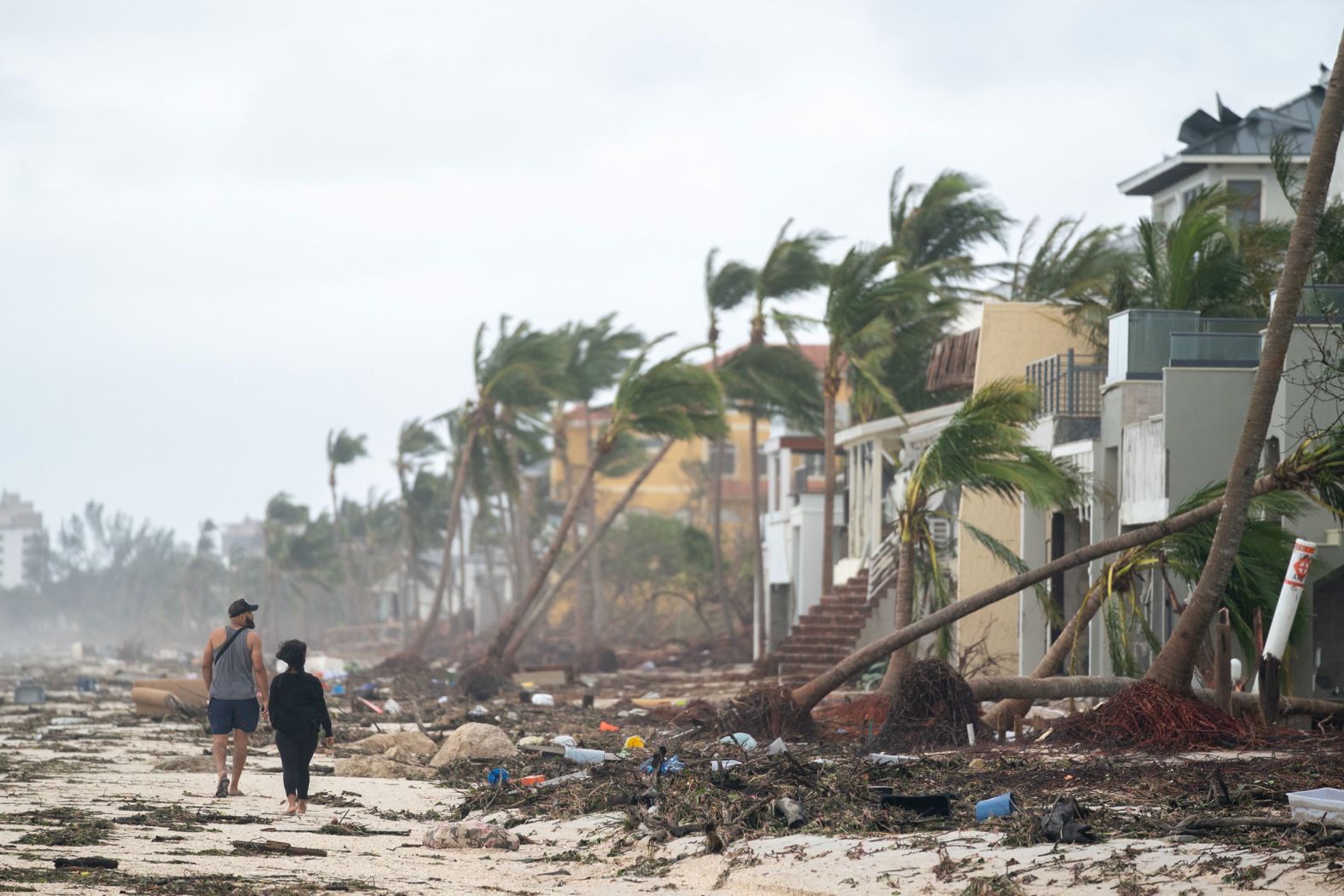 People walk along the beach looking at property damaged in Bo