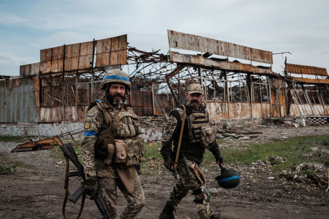 Ukrainian servicemen walk past a destroyed building in Kyrylivka, in the recently retaken area near Kharkiv, on September 30, 2022.