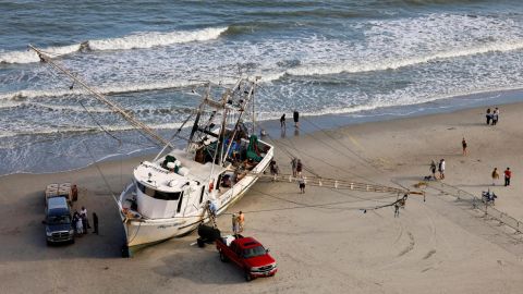 Workers and owners of a large shrimping boat prepare their vessel for towing back into the water Saturday after it was swept ashore in Myrtle Beach, South Carolina.