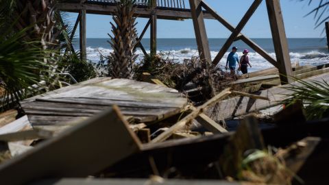 A couple walks past damage from Hurricane Ian on Litchfield Beach, South Carolina on October 1, 2022.