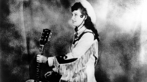 Loretta Lynn porte un chapeau de cow-boy et une veste de style western à franges tout en tenant une guitare acoustique alors qu'elle pose pour un portrait vers 1960 à Nashville, Tennessee. 