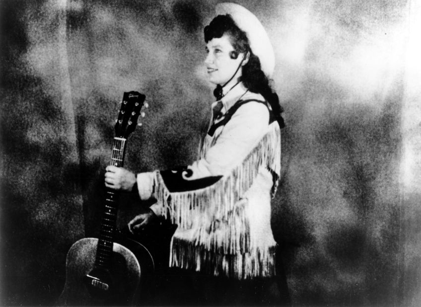 Lynn wears a cowboy hat and a fringe western style jacket while holding an acoustic guitar in Nashville circa 1960. 
