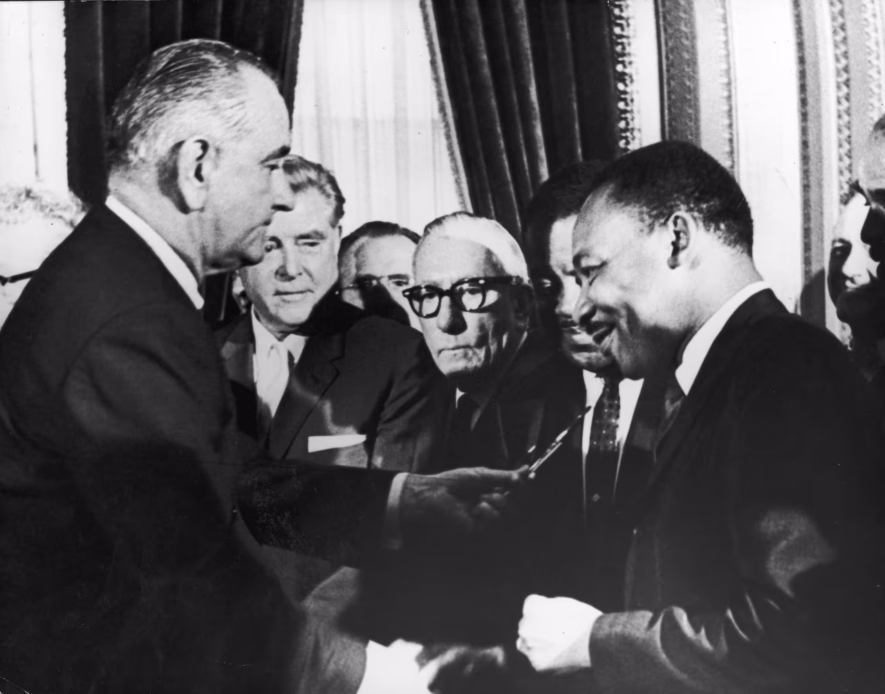 US President Lyndon B Johnson hands a pen to civil rights leader Reverend Martin Luther King Jr during the the signing of the voting rights act as officials look on behind them, Washington DC, August 6, 1965. (Photo by Washington Bureau/Getty Images)