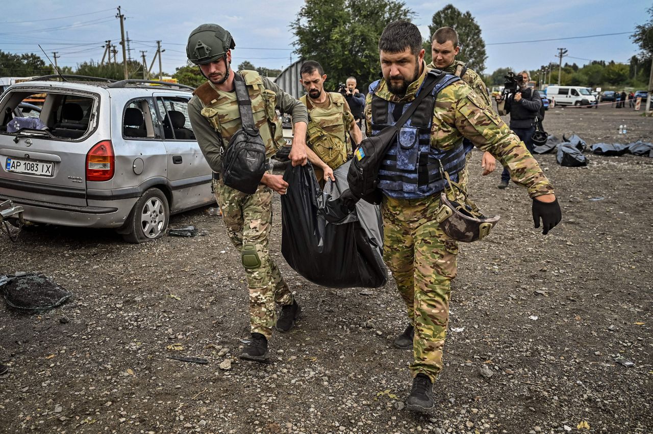 Ukrainian servicemen carry a body bag at the site of a missile <a target=
