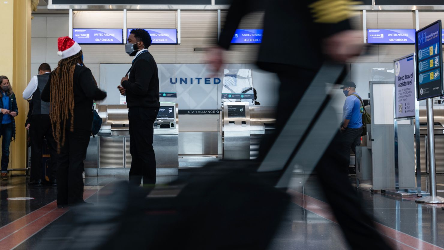 An airline crew member rolls their bag past the United Airlines ticket counter at Reagan National Airport in Arlington, Virginia, U.S., on Friday, Dec. 24, 2021. Air carriers scrapped more than 800 U.S. flights for the holiday weekend, led by United Airlines and Delta Air Lines, as surging Covid infections and the prospects of bad weather disrupted Christmas travel. Photographer: Eric Lee/Bloomberg via Getty Images