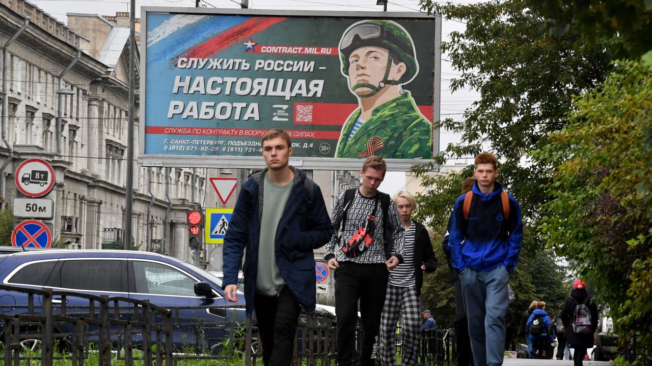 Young men walk in front of a billboard promoting contract army service with an image of a serviceman and the slogan reading "Serving Russia is a real job" in Saint Petersburg on September 29, 2022. - Russian President Vladimir Putin announced on September 21 a mobilisation of hundreds of thousands of Russian men to bolster Moscow's army in Ukraine, sparking demonstrations and an exodus of men abroad. (Photo by Olga MALTSEVA / AFP) (Photo by OLGA MALTSEVA/AFP via Getty Images)
