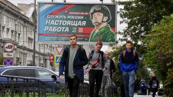 Young men walk in front of a billboard promoting contract army service with an image of a serviceman and the slogan reading "Serving Russia is a real job" in Saint Petersburg on September 29, 2022. - Russian President Vladimir Putin announced on September 21 a mobilisation of hundreds of thousands of Russian men to bolster Moscow's army in Ukraine, sparking demonstrations and an exodus of men abroad. (Photo by Olga MALTSEVA / AFP) (Photo by OLGA MALTSEVA/AFP via Getty Images)