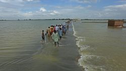 TOPSHOT - Stranded people wade through a flooded area after heavy monsoon rainfall in Rajanpur district of Punjab province on August 25, 2022. - Figures from the national disaster agency showed on August 25 that 903 people had died in the floods since June, and over 180,000 were forced to flee their rural homes. (Photo by Shahid Saeed MIRZA / AFP) (Photo by SHAHID SAEED MIRZA/AFP via Getty Images)