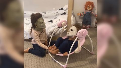 Aubriella pushes her younger brother Dominic in a baby bouncer, both wearing Michael Myers masks. 