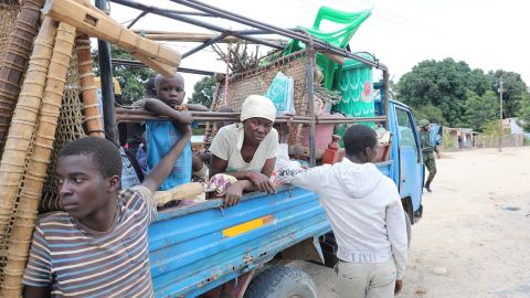 A family sitting in the back of a pick-up truck with their belonging as they return to their village.
