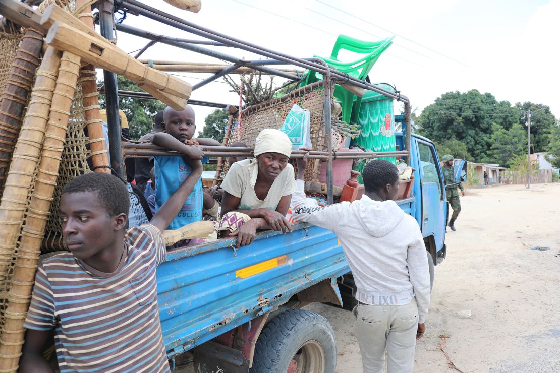 A family sitting in the back of a pick-up truck with their belonging as they return to their village.
