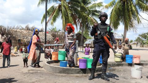 A Rwandan Policeman stands guard as women and children pump water out of well in the village of Olumbi in Cabo Delgado province in Mozambique in Sep. 2022.
