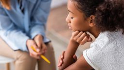 Close up of upset african american girl with closed eye near psychologist during consultation on blurred background