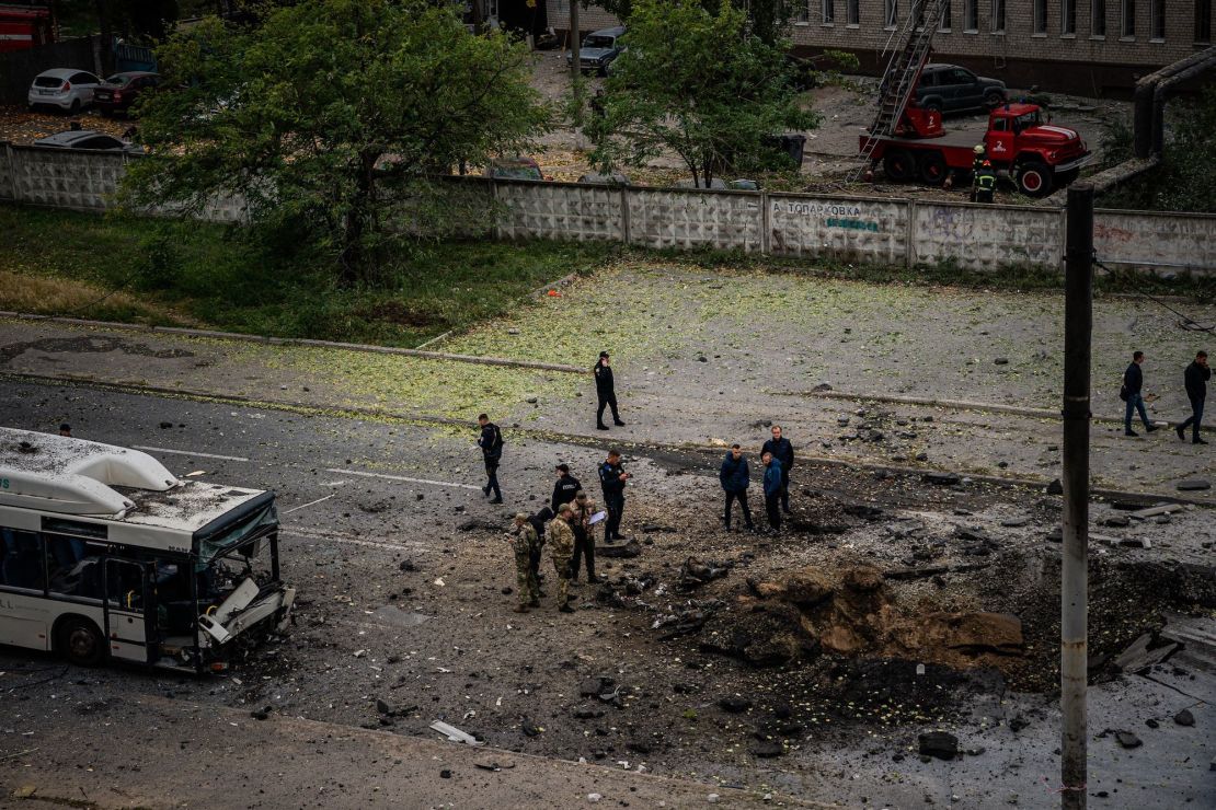 Investigators examine a crater next to a damaged bus following a missile strike in Dnipro on Monday.