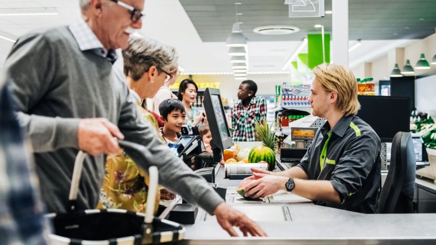 A cashier ringing up a senior couple's groceries so they can pay at their local supermarket.