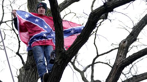 A Donald Trump supporter holds a Confederate flag while atop a tree during a January 6, 2021, rally in Washington, DC.