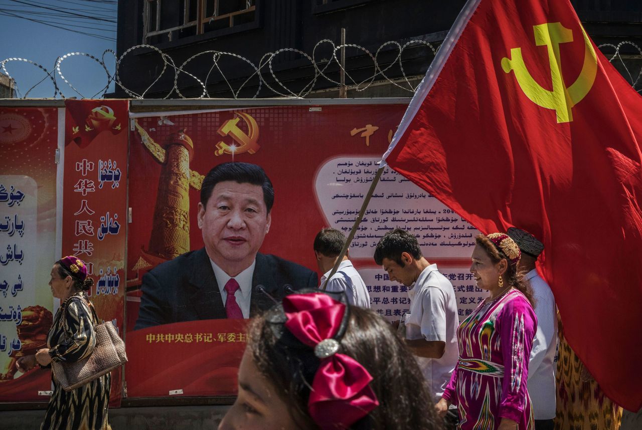 Ethnic Uyghur members of the Communist Party of China carry a flag past a billboard of Xi in Kashgar, China, in June 2017.
