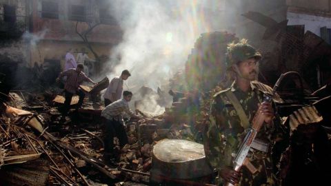 An Indian Muslim family searches for valuables from their burnt down house while an Indian Army soldier stands guard March 3, 2002 in downtown Ahmedabad, India.