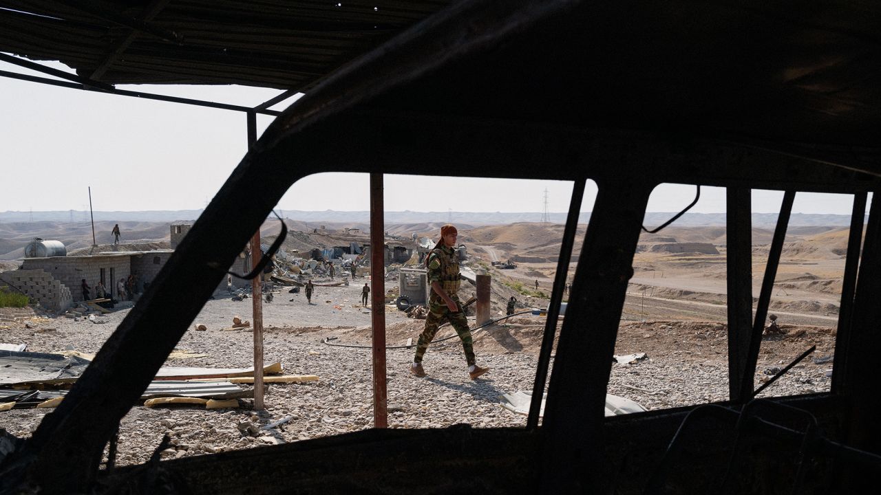 A man walks past the carcass of a vehicle weeks after it was attacked by Iranian drones and missiles.