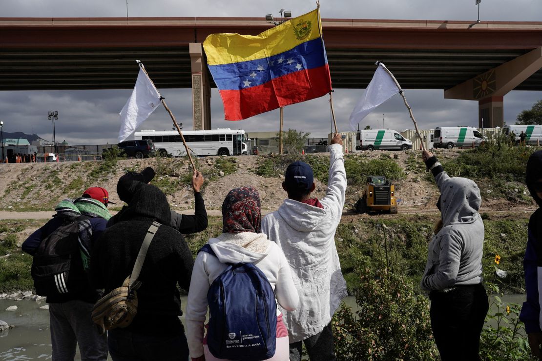 Venezuelan migrants, some who were expelled back to Mexico, and others who arrived in Juarez and haven't crossed yet, wave flags on the banks of the Rio Grande Tuesday while peacefully protesting new US migration enforcement rules.