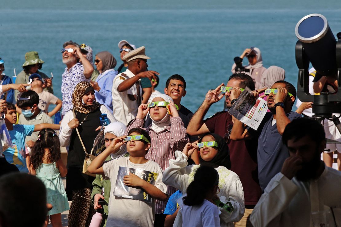 People wearing protective glasses and equipment take a glimpse of a partial solar eclipse in Kuwait City on Tuesday.  