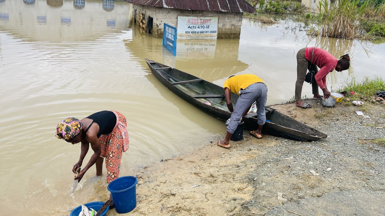 Chigozie Uzo (L), a displaced resident of Odi, in Nigeria's southern Bayelsa State rinses her uncooked fish in dirty floodwater, Tuesday.