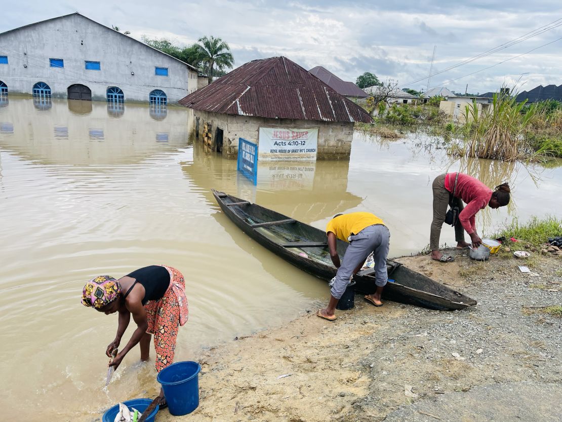 Chigozie Uzo (L), a displaced resident of Odi, in Nigeria's southern Bayelsa State rinses her uncooked fish in dirty floodwater, Tuesday.